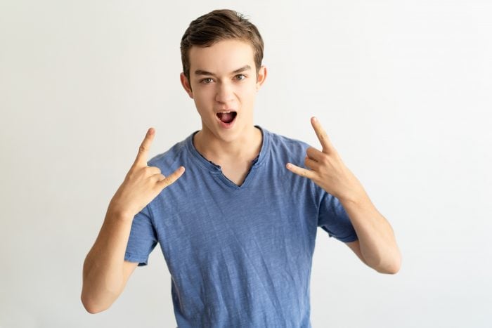 Young man with fists closed and the index and little fingers up, making the horns hand sign