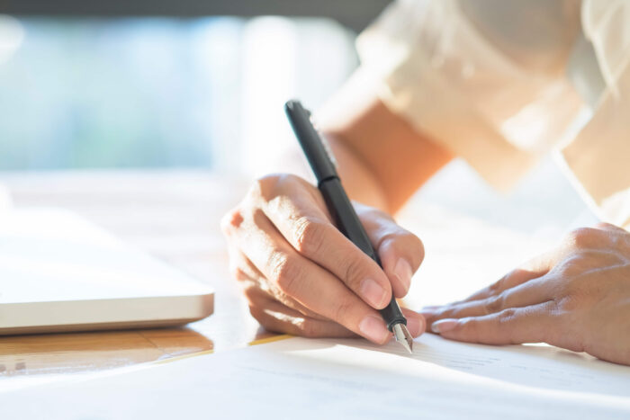 Hand with pen writing the written part of the English language test for citizenship in the UK.