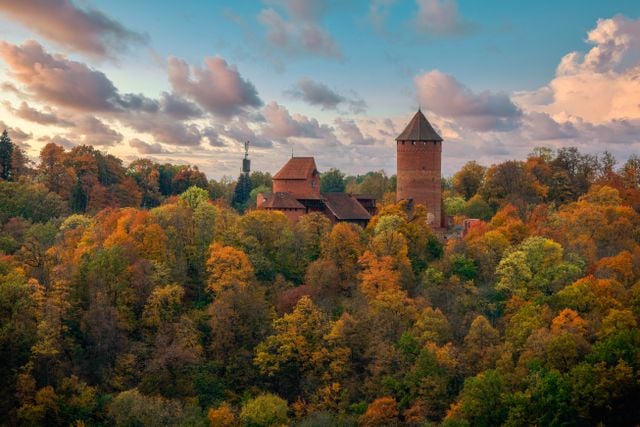 1. Historic Lithuanian castle surrounded by colourful autumn forest, reflecting the landscape and heritage of Lithuania.