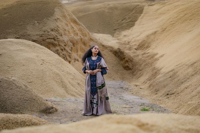 Amazigh woman wearing traditional dress in a mountainous North African landscape.