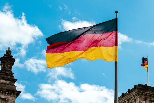 German flag flying outside a government building under a blue sky.