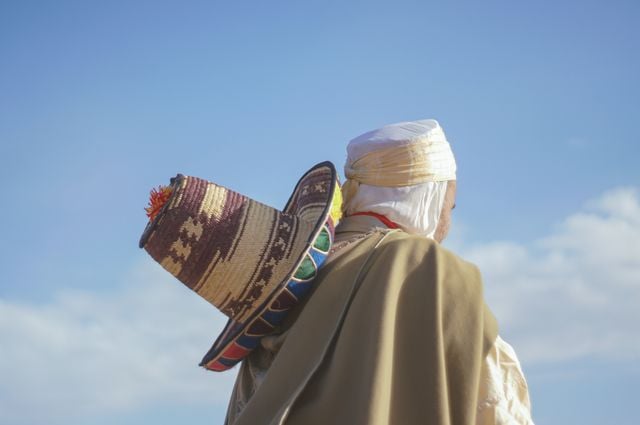 Amazigh person wearing traditional clothing and carrying a woven basket under a clear blue sky.