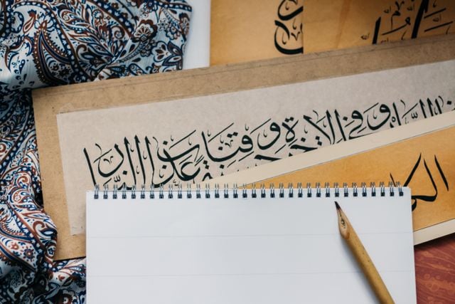 Arabic calligraphy displayed alongside a blank notebook and pencil, illustrating the beauty of written Arabic.